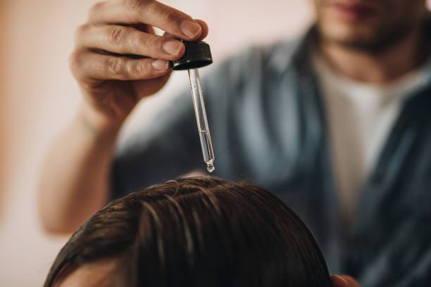 close up of a hairdresser applying hair oil on customer's hair at the salon.